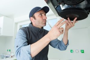 Image of a handyman replacing a carbon charcoal filter from an undercabinet range hood. Source: Adobe Stock