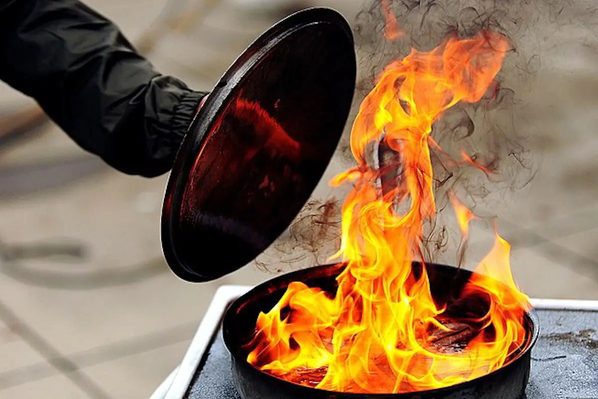 Image of a person putting out a grease fire with a pan lid. Source: wiki commons.