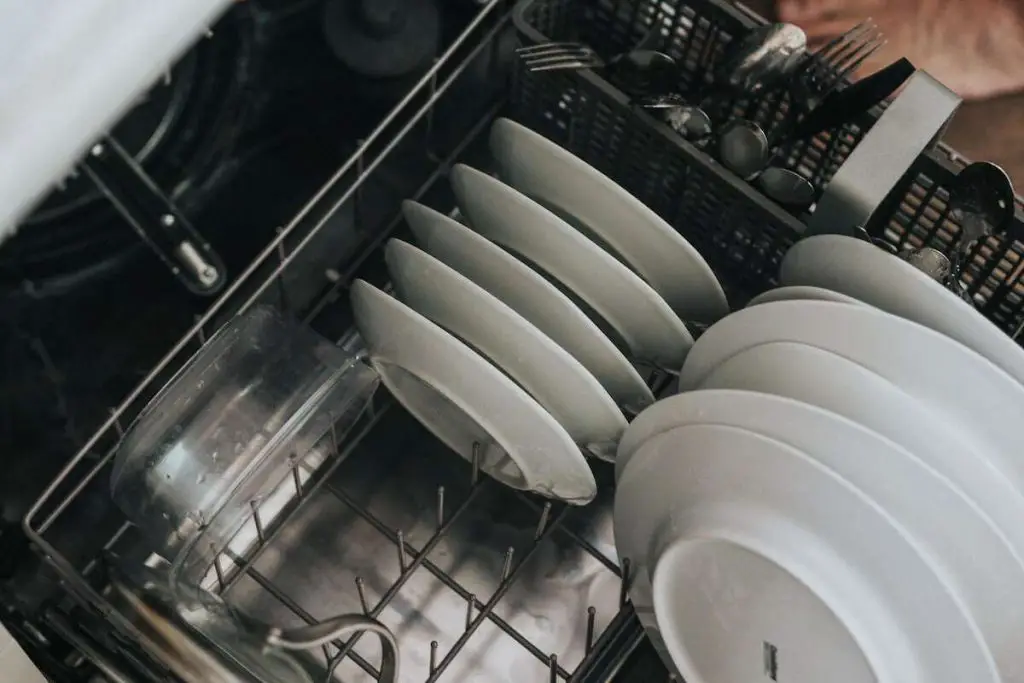 Man loading dishwasher with white plates.