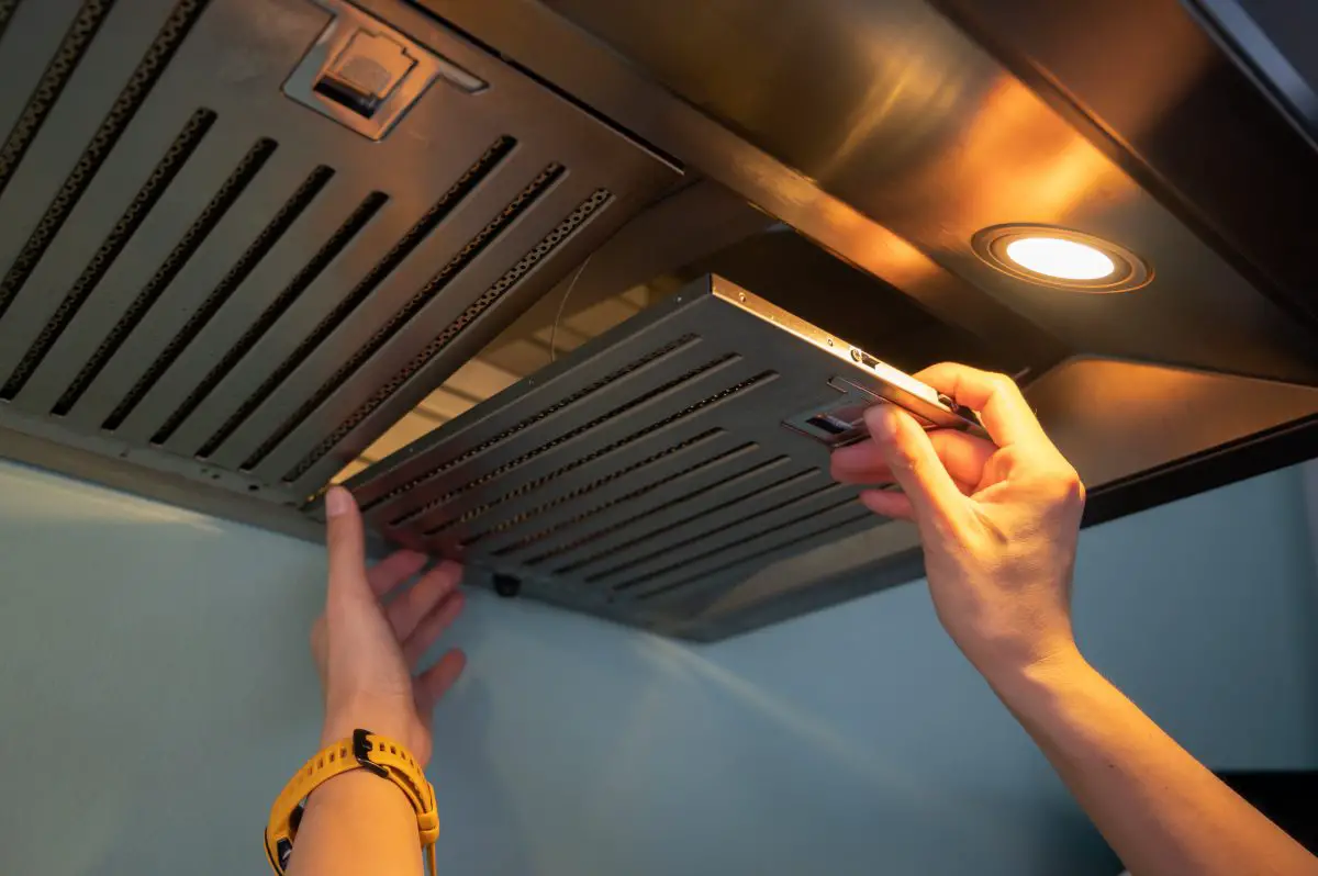 Image of a woman replacing a baffle filter on a wall mount range hood. Source: adobe stock