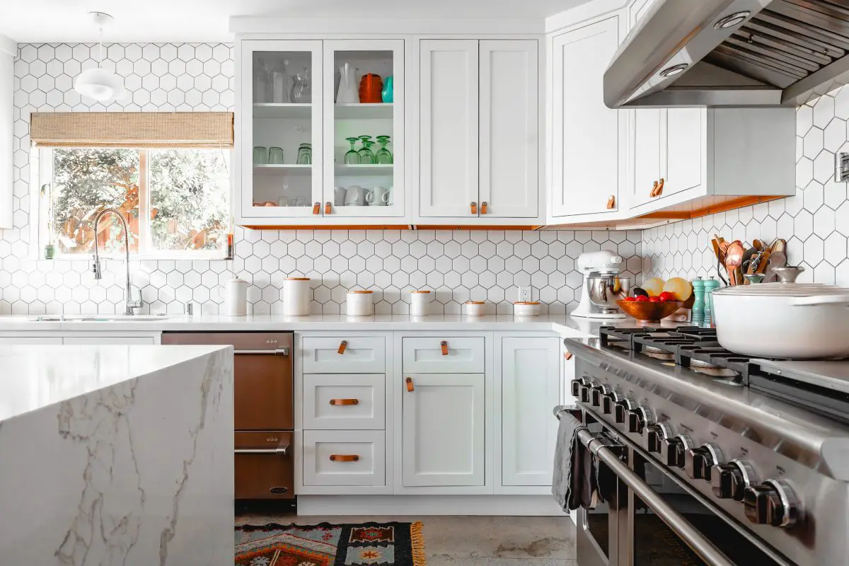 Image of a clean white painted kitchen with a range hood over a stove. Source: roam in color, unsplash