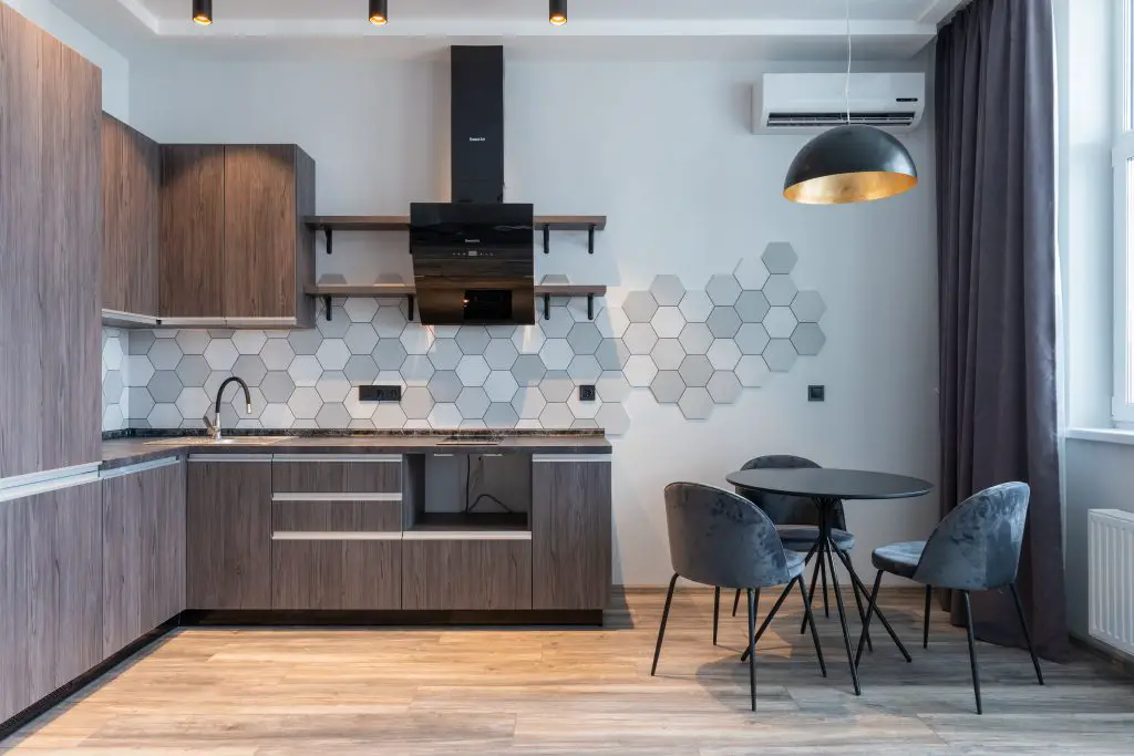 Image of a kitchen with wooden cabinets a range hood a table and three chairs. Source: max, vakhtbovych pexels