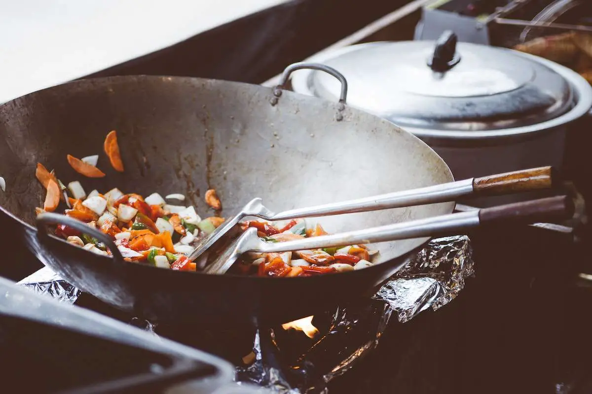 Image of a black wok cooking vegetables in kitchen.