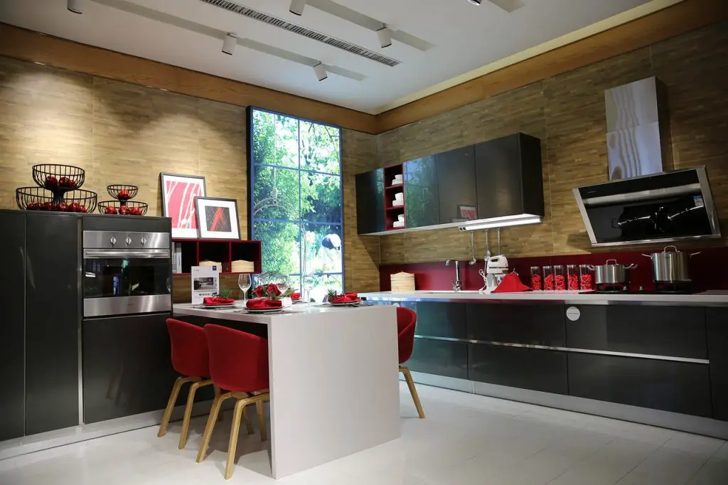 Image of a kitchen with a table and red chairs, a countertop, a stove, and a range hood. Source: pixabay