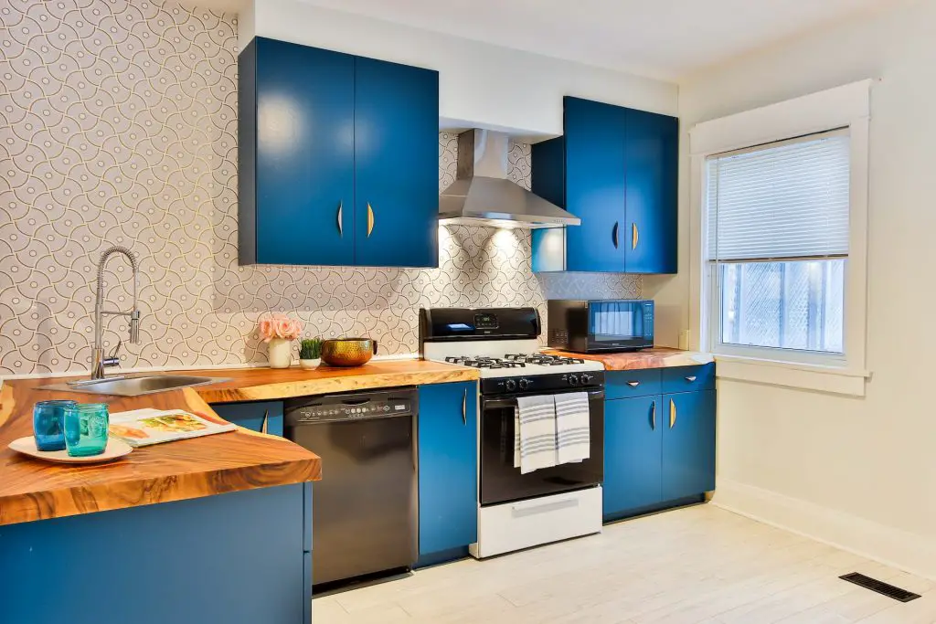 Image of a kitchen with a wooden countertop, blue cabinets, a stove, and a range hood on top of it. Source: sidekix media, unsplash