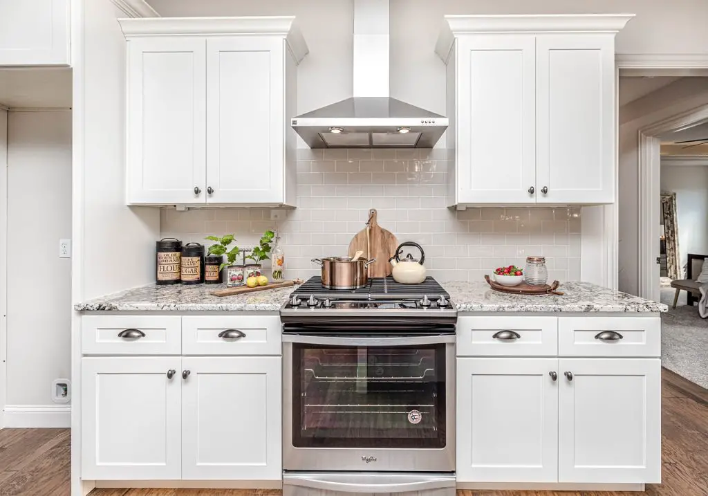Image of a kitchen with white cabinets, a marble design countertop, a stove, and a range hood above it. Source: pixabay