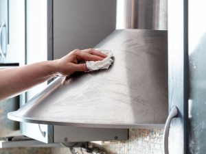 Image of a person washing the surface of a stainless steel range hood. Source: Adobe Stock