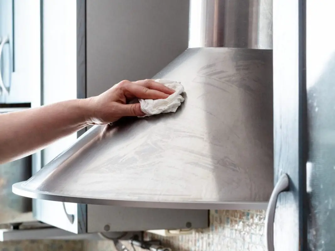 Image of a person washing the surface of a stainless steel range hood. Source: adobe stock