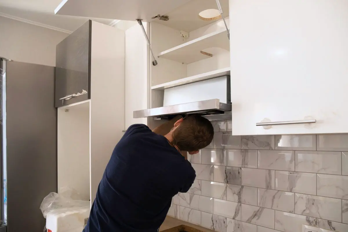 Image of a man with dark blue shirt installing a ductless range hood. Source: adobe stock