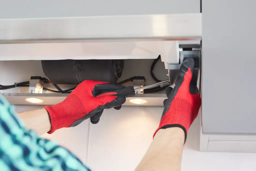 Image of a person repairing a range hood with red gloves. Source: Adobe Stock