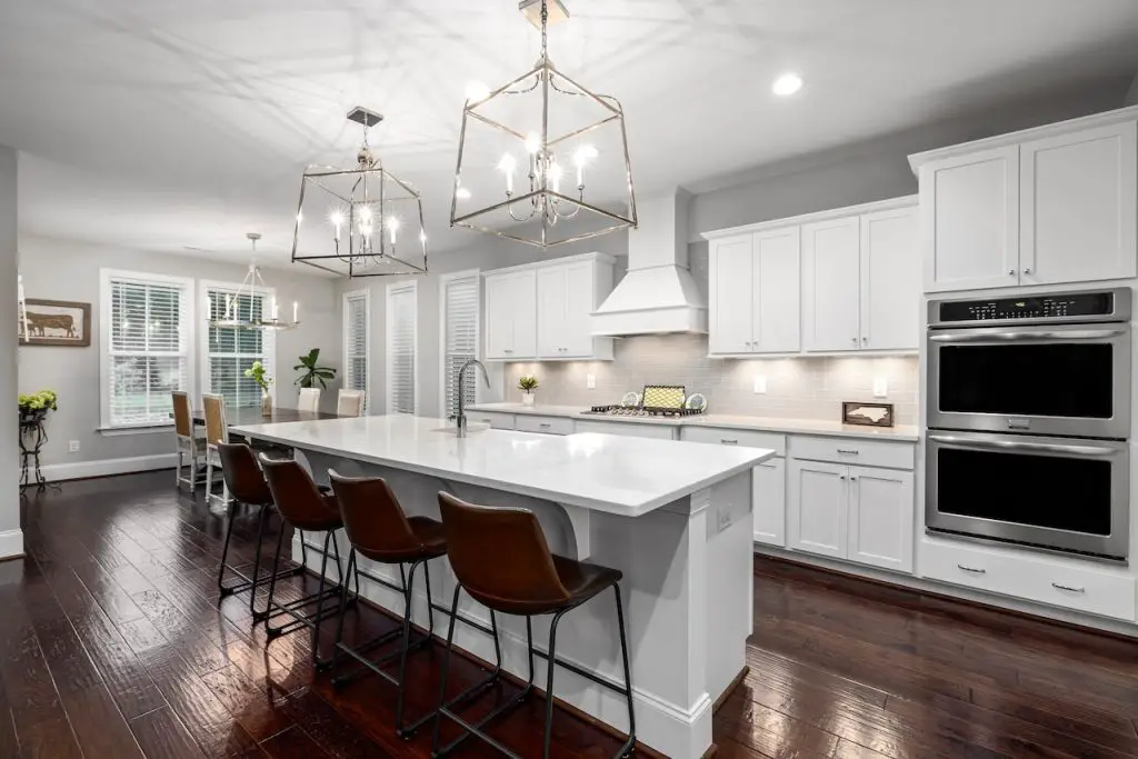 Image of a white painted kitchen, a counter top with chairs, and a range hood. Source: curtis adams, pexels